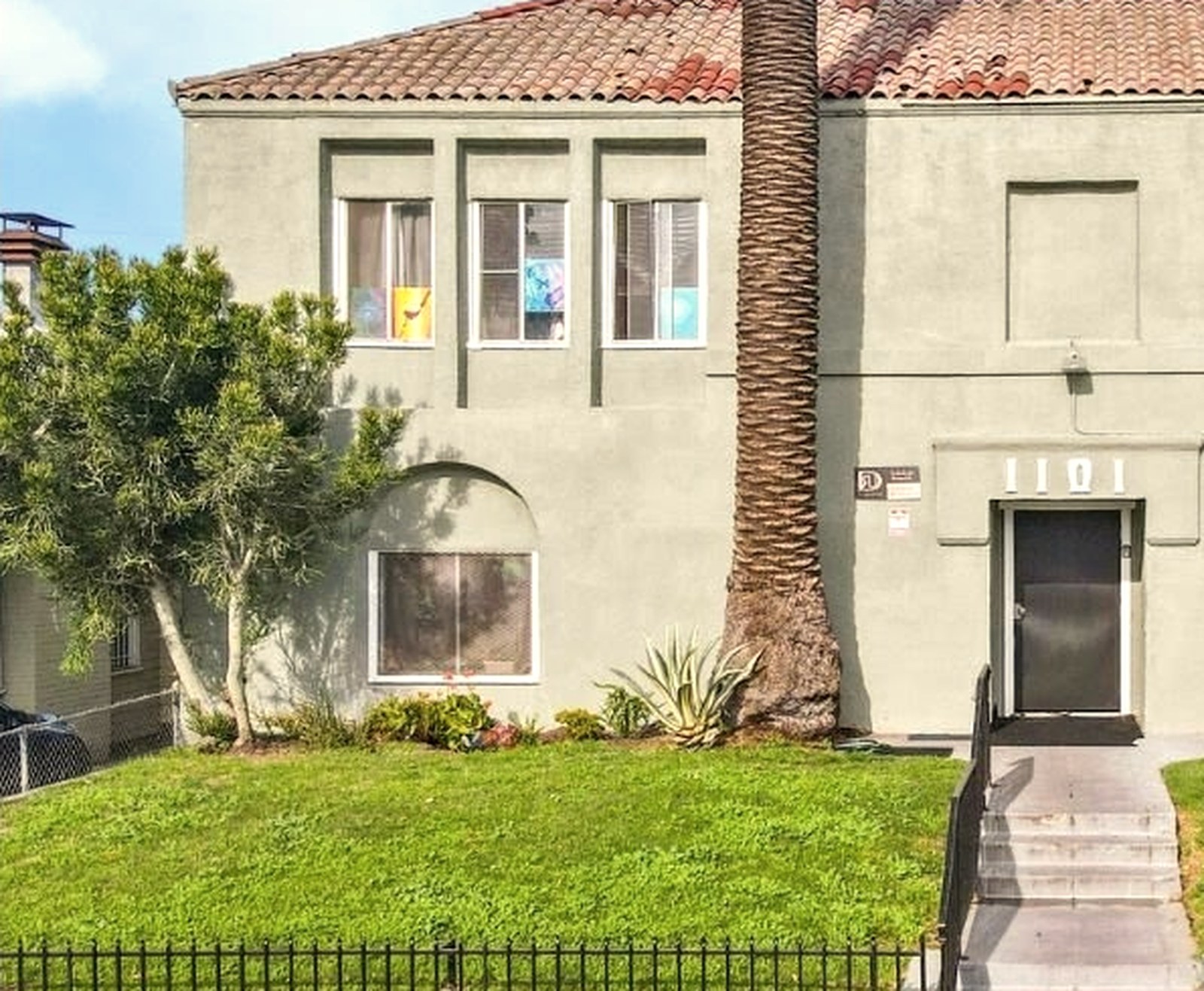 1101 W 45th Street, a two-story Spanish-tile-roof 20-unit apartment building in Historic South Central Los Angeles 90037, with stucco walls, a mature palm, and an olive tree in the front yard.